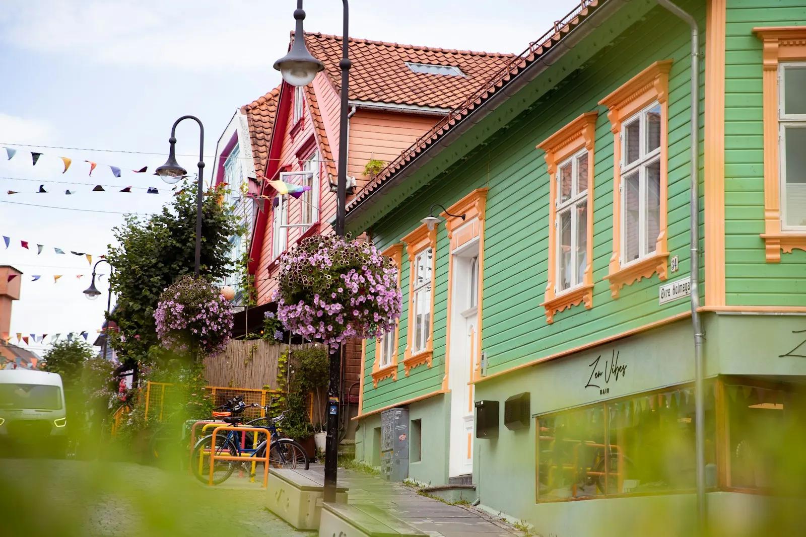 Grønt trehus med oransje vinduslister og blomsterampler i en gate i Stavanger